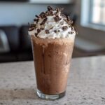 A tall glass of creamy frozen hot chocolate topped with whipped cream and chocolate shavings.