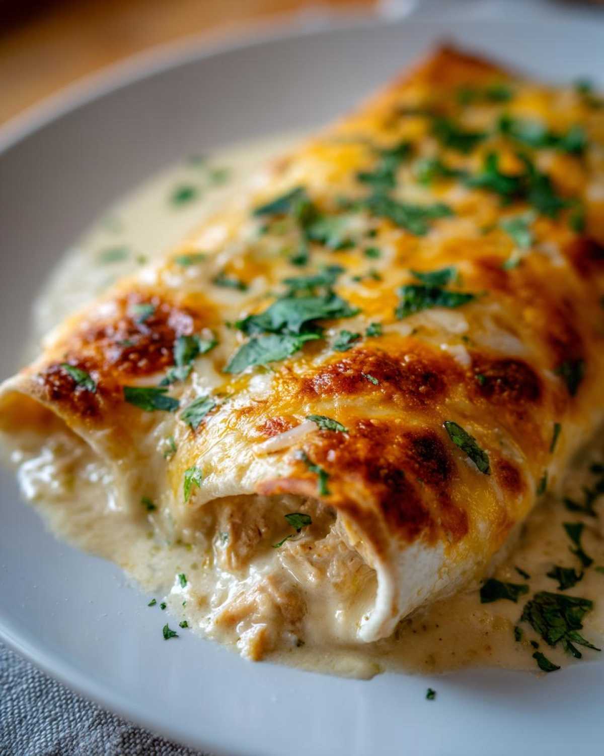 Close-up of a cheesy, creamy green chile chicken enchiladas smothered in sauce and topped with cilantro.