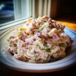 A close-up of a generous serving of creamy ham salad recipe, featuring diced ham and celery, in a white bowl.