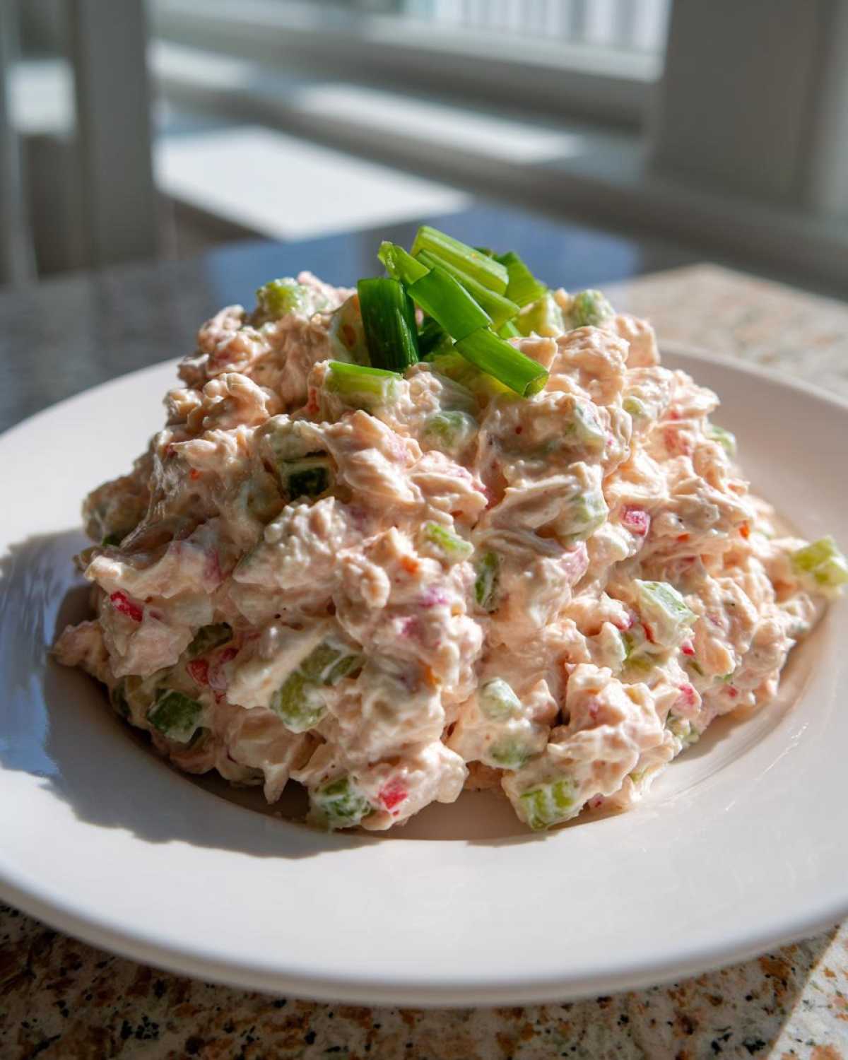 A generous mound of creamy ham salad recipe mixed with celery and red pepper, garnished with chopped green onions.