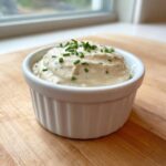 A small white ramekin filled with thick, creamy horseradish sauce, topped with chopped chives.