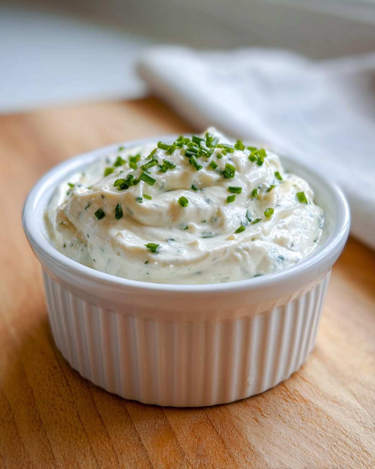 A white ramekin filled with thick, creamy horseradish sauce, topped with fresh chopped chives.