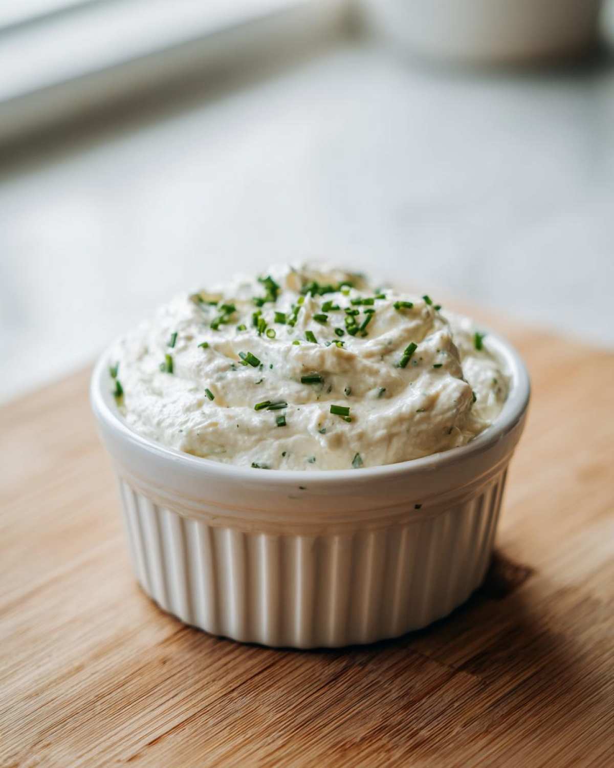 A white ramekin filled with thick, creamy horseradish sauce, topped with fresh chopped chives.