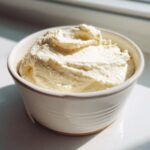 A close-up of thick, creamy horseradish sauce served in a small white bowl, brightly lit by sunlight.