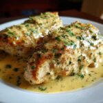 Two seared chicken breasts smothered in a rich, creamy lemon sauce and topped with fresh parsley.