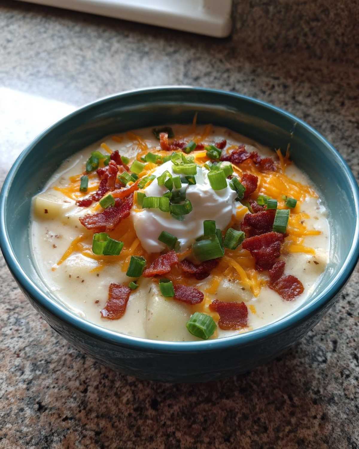A close-up of a bowl of creamy loaded baked potato soup topped with shredded cheese, bacon bits, sour cream, and green onions.