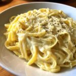 Close-up of fettuccine pasta coated in rich olive garden alfredo sauce, topped with Parmesan and black pepper.