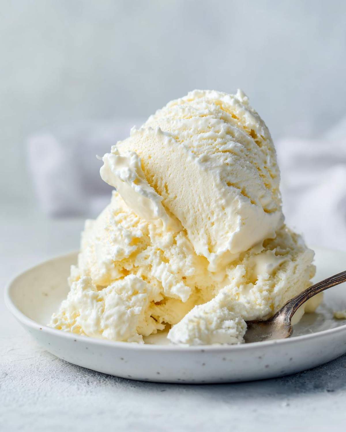 Close-up of two scoops of creamy vanilla protein ice cream served in a speckled white bowl with a small spoon.