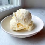 Two scoops of creamy, pale yellow protein ice cream served in a small white bowl.