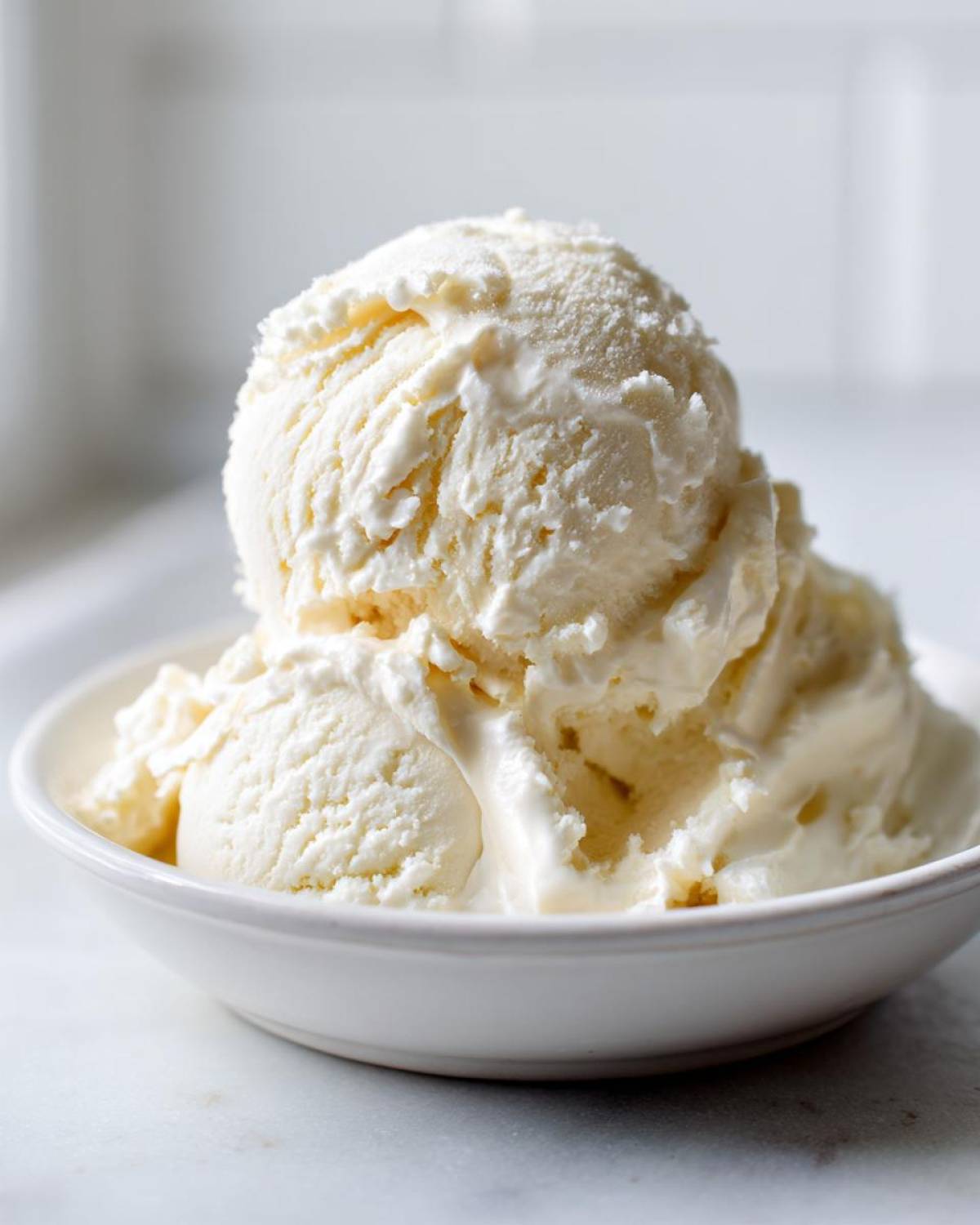 Close-up of three scoops of creamy vanilla protein ice cream in a white bowl.