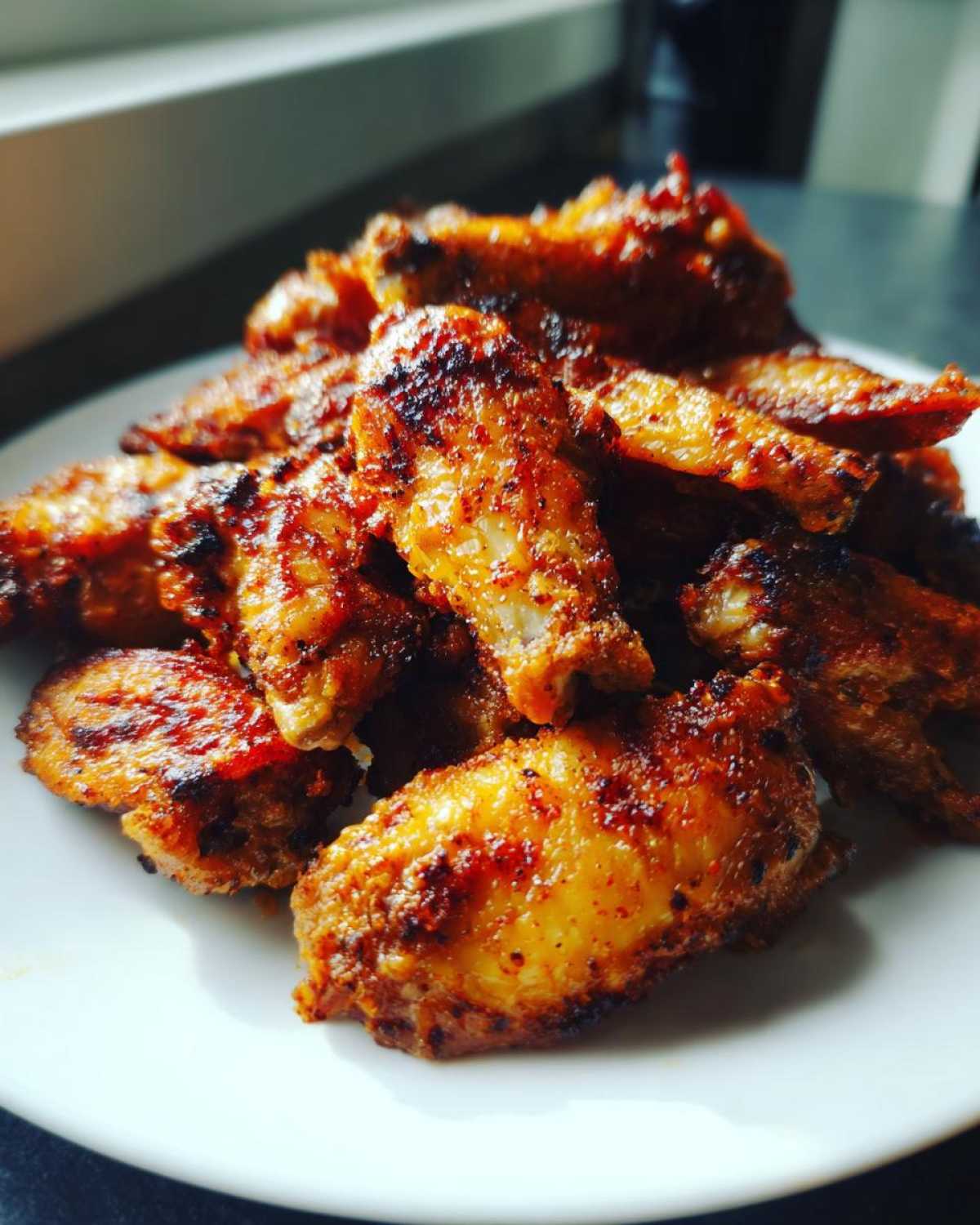 A close-up of a pile of perfectly seasoned and crispy baked chicken wings on a white plate.