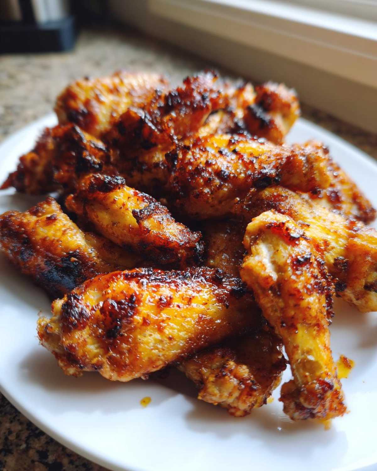 A close-up of golden brown, perfectly seasoned and crispy baked chicken wings piled on a white plate.