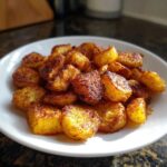 A close-up of a pile of golden brown, crispy breakfast potatoes seasoned with spices, served on a white plate.