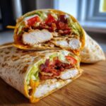 A cross-section view of a delicious chicken bacon ranch wrap, showing crispy chicken, bacon, lettuce, and ranch dressing.