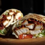 Close-up of a crispy chicken bacon ranch wrap cut in half, showing layers of chicken, bacon, lettuce, and ranch dressing.