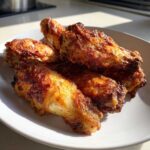 Close-up of several golden brown, crispy chicken wing pieces piled on a white plate.