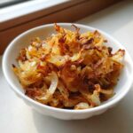 A white bowl filled with crispy, golden-brown fried onions, a perfect topping for fried potatoes.