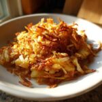 A close-up of perfectly golden brown and crispy fried potatoes piled high on a white plate.