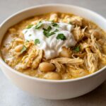 Close-up of a bowl of creamy crockpot white chicken chili featuring shredded chicken, white beans, and a dollop of sour cream garnished with parsley.