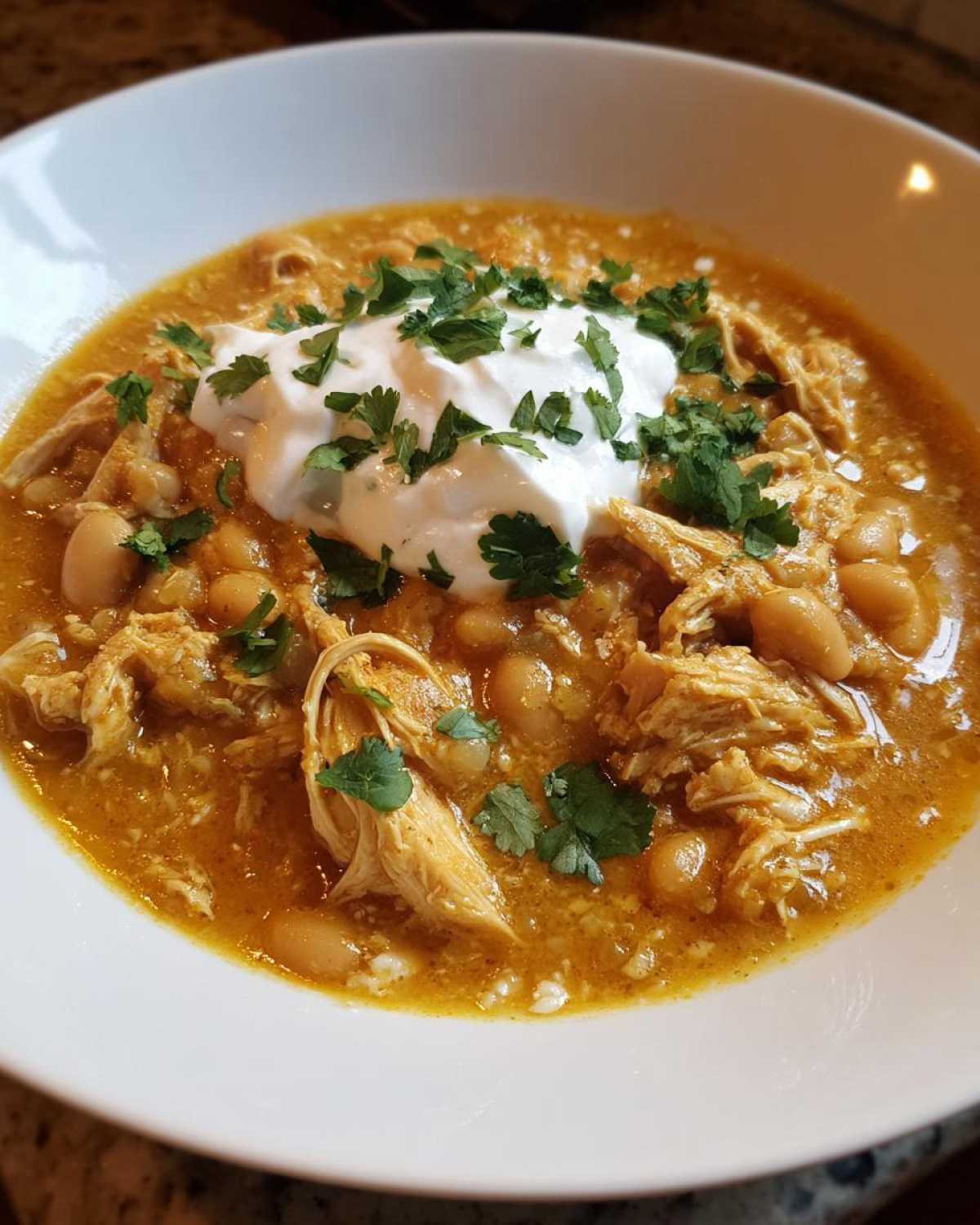 Close-up of a bowl of rich crockpot white chicken chili, topped with sour cream and fresh cilantro.