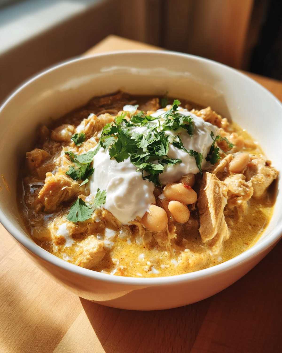 A close-up of a bowl of creamy crockpot white chicken chili topped with sour cream and fresh cilantro.