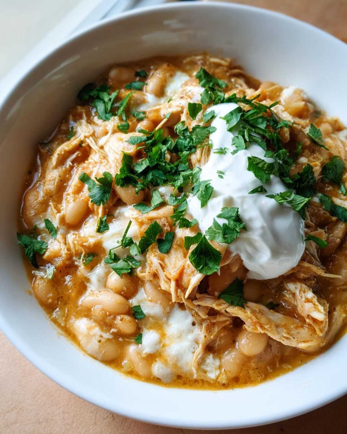Close-up of a hearty bowl of crockpot white chicken chili topped with sour cream and fresh parsley.