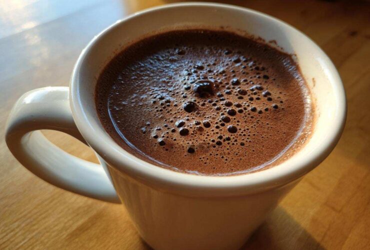 Close-up of a white mug filled with rich, foamy hot cocoa mix, sitting on a wooden table.