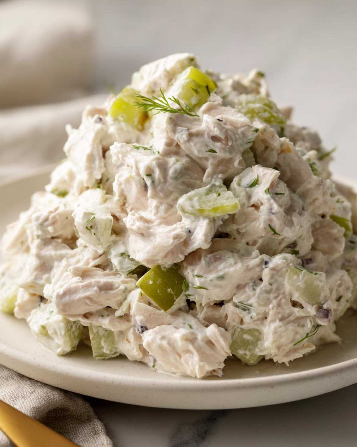 A mound of creamy dill pickle chicken salad featuring chunks of chicken and bright green pickle pieces, garnished with fresh dill.