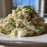 Close-up of a creamy mound of dill pickle chicken salad mixed with green pickle pieces, garnished with fresh dill.
