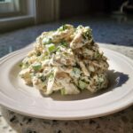 A mound of creamy dill pickle chicken salad garnished with fresh dill, served on a white plate.