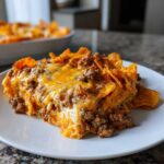 A close-up serving of cheesy Dorito Casserole topped with seasoned ground beef and melted cheddar cheese.
