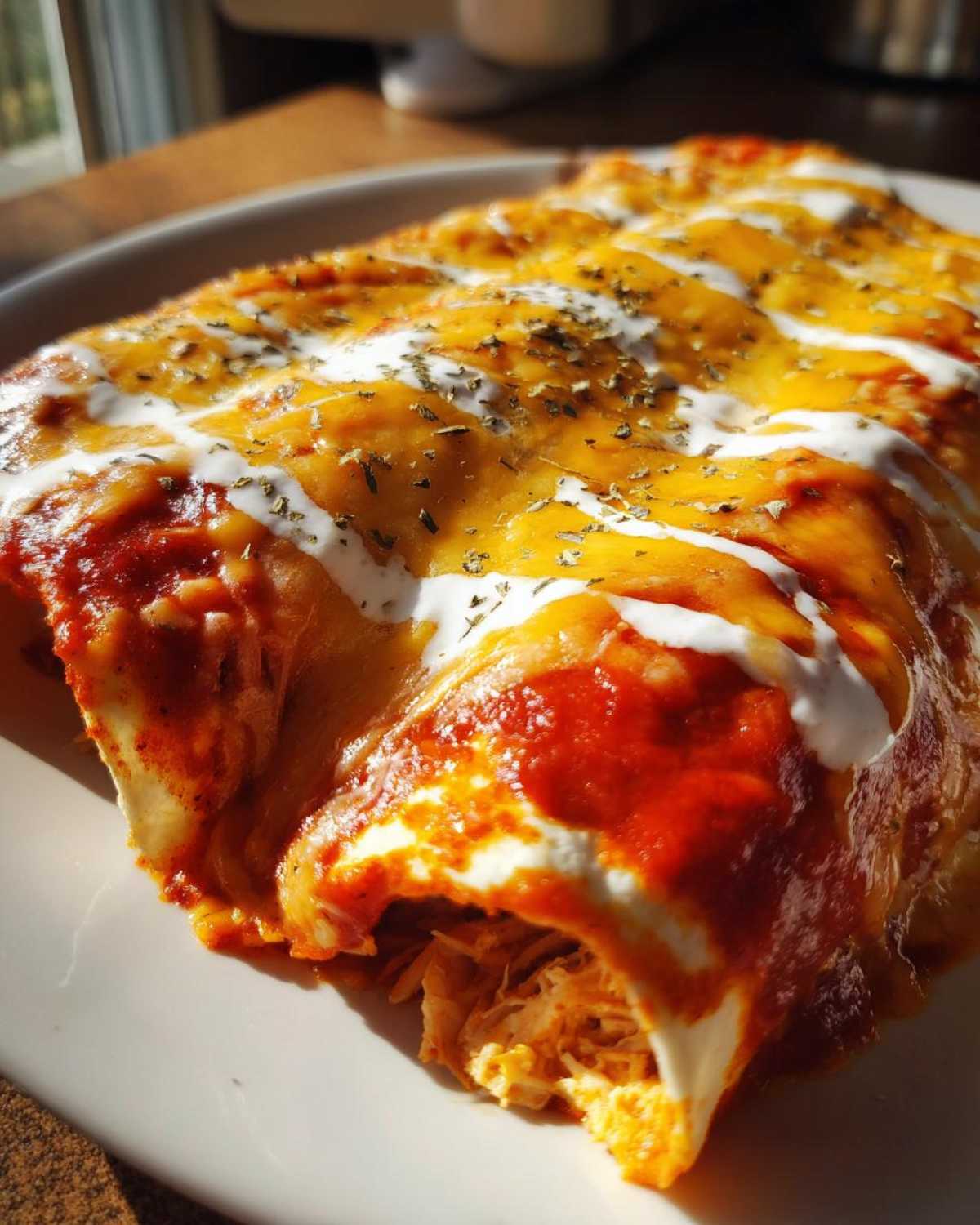 Close-up of baked easy chicken enchiladas covered in red sauce, melted cheddar, sour cream, and herbs.