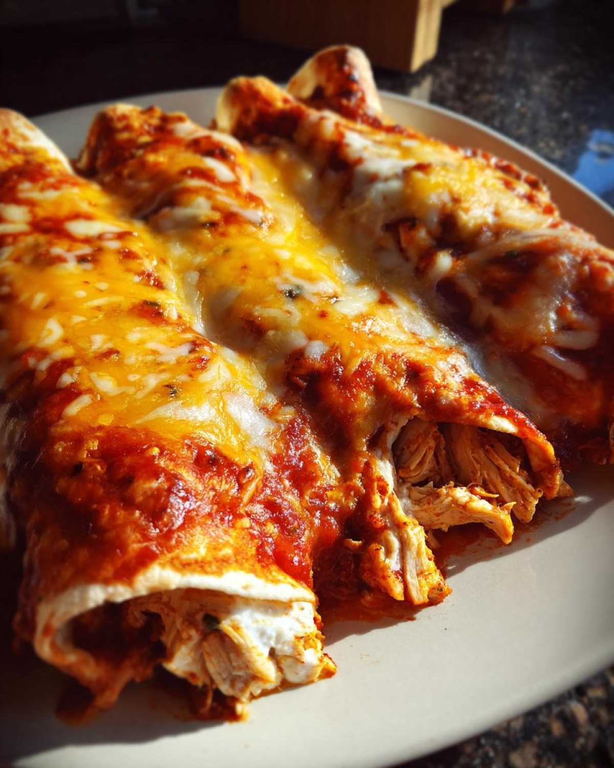 Close-up of three easy chicken enchiladas covered in red sauce and melted orange and white cheese.