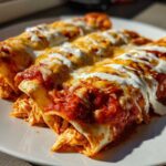 Close-up of three rolled easy chicken enchiladas covered in red sauce, melted cheese, and sour cream.