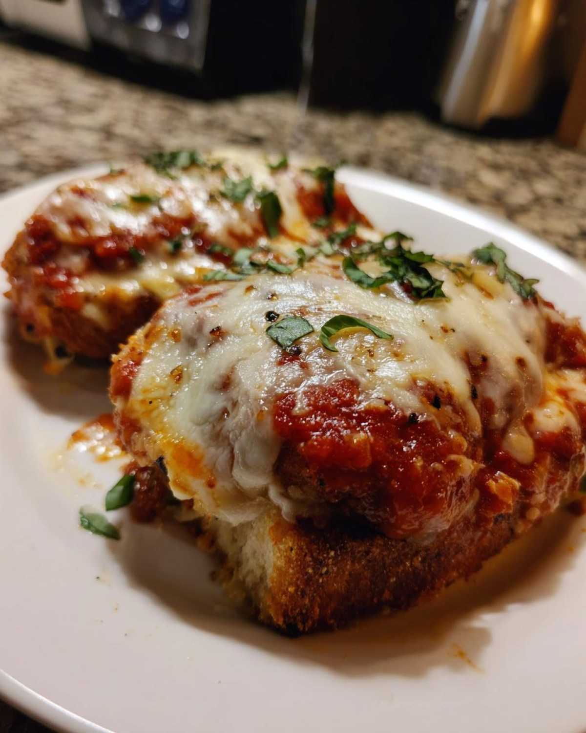 Two portions of Easy Chicken Parmesan topped with melted mozzarella, marinara sauce, and fresh basil.