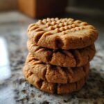 A close-up stack of three classic Easy Peanut Butter Cookies with fork marks on top, resting on a granite counter.