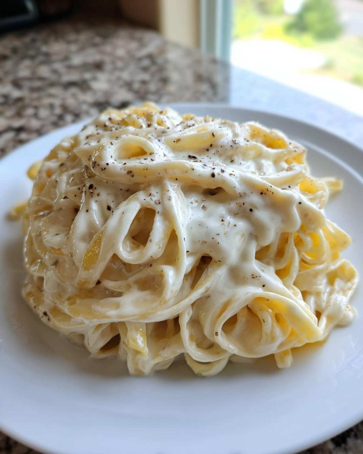 A close-up of fettuccine pasta generously coated in creamy homemade alfredo sauce and topped with black pepper.