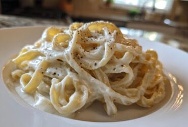 Close-up of fettuccine pasta coated in rich homemade alfredo sauce and topped with black pepper.