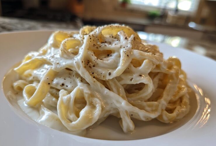 Close-up of fettuccine pasta coated in rich homemade alfredo sauce and topped with black pepper.
