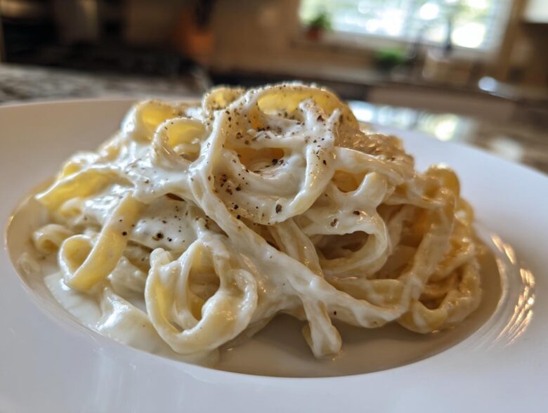 Close-up of fettuccine pasta coated in rich homemade alfredo sauce and topped with black pepper.