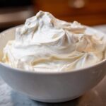 Close-up of thick, bright white, fluffy icing mixture in a white bowl, ready for decorating using the royal icing recipe.