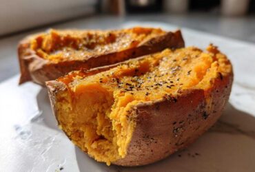 Close-up of a perfectly baked sweet potato cut in half, showing the fluffy orange interior seasoned with pepper.
