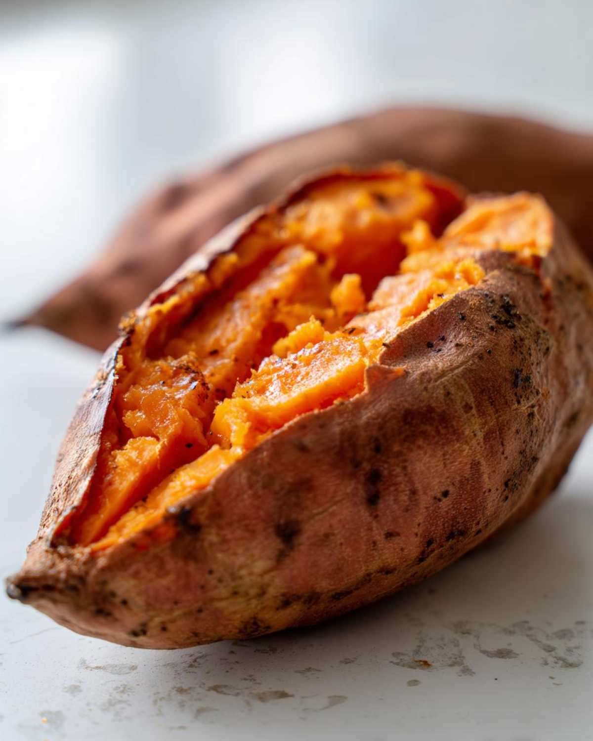 Close-up of a perfectly baked sweet potato split open to show the soft, bright orange interior flesh.