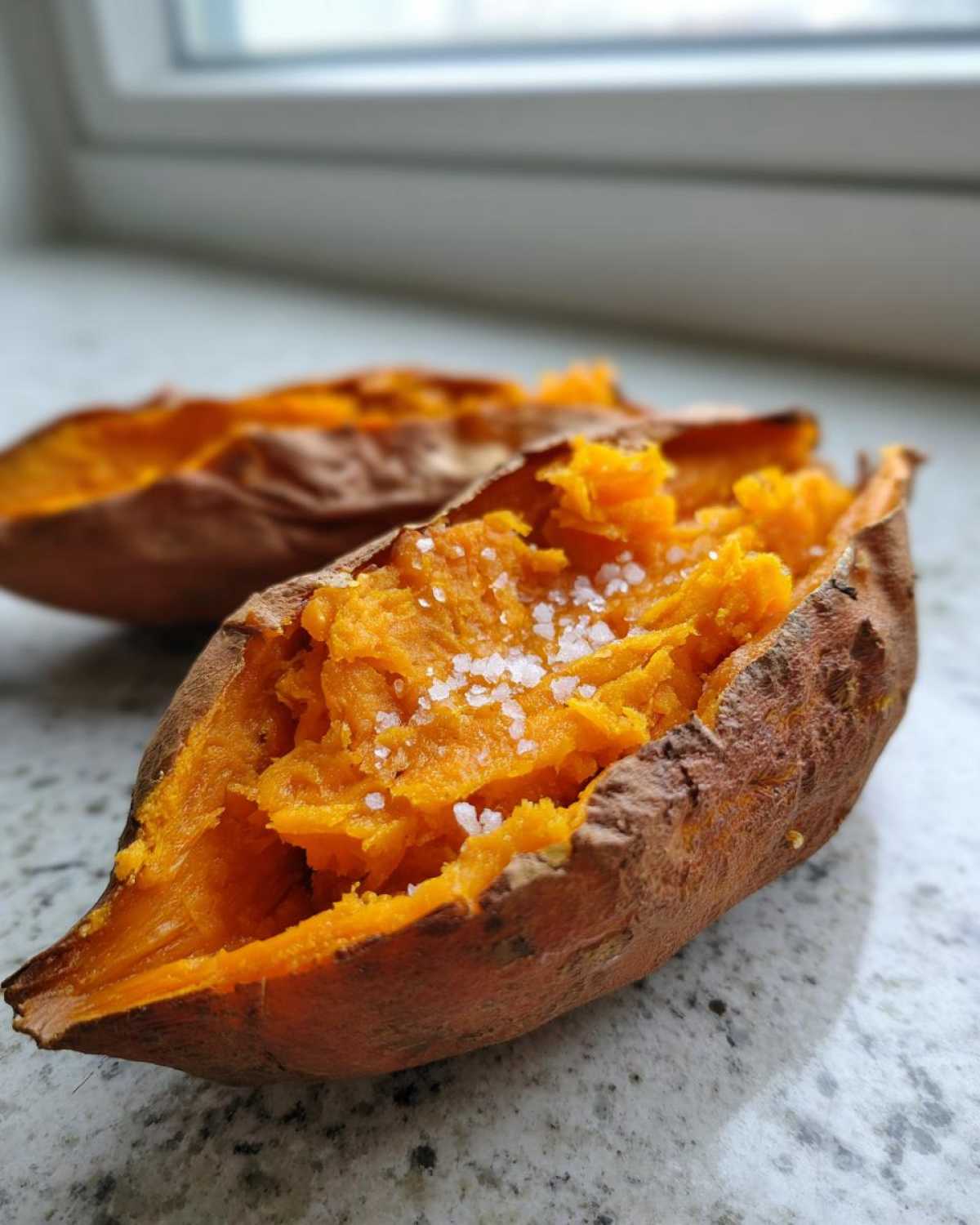 Close-up of a perfectly baked sweet potatoes, split open and topped with coarse sea salt.