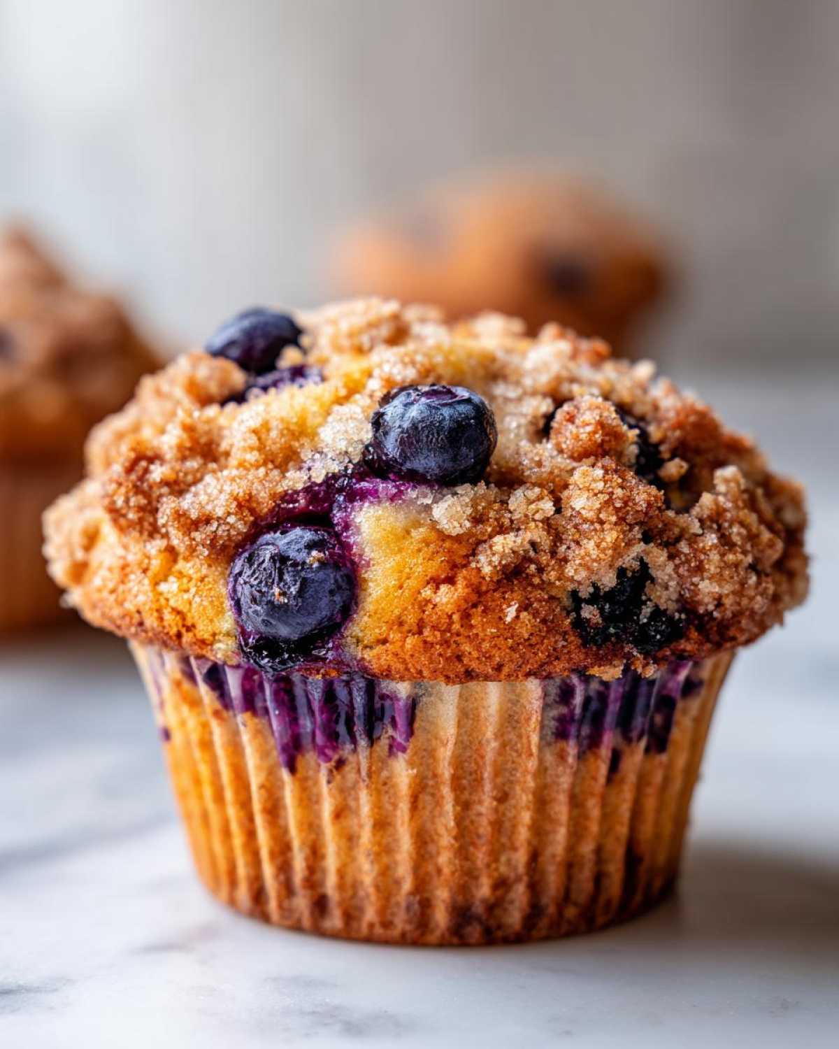 Close-up of a perfectly baked blueberry muffin with a golden crumb topping and visible fresh blueberries.