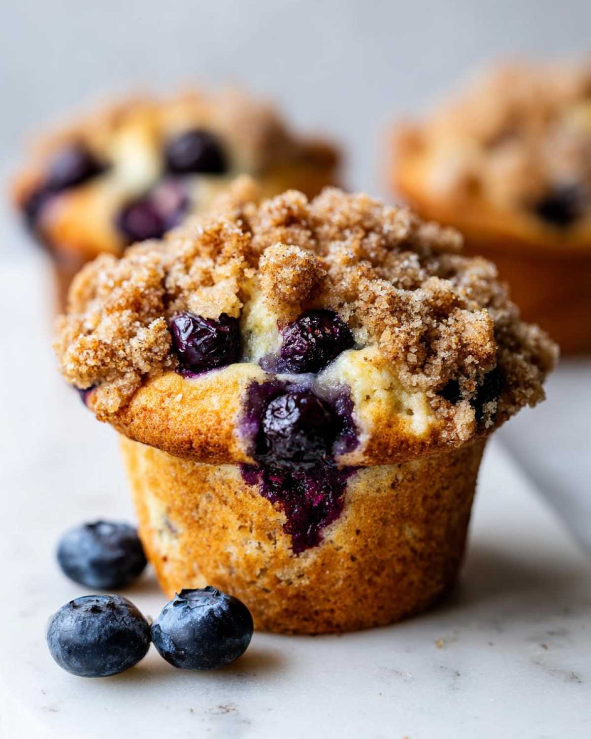 Close-up of a fluffy blueberry muffin topped with brown sugar streusel, with fresh blueberries nearby.