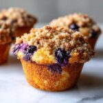 A close-up shot of a golden brown blueberry muffin topped with crunchy streusel, highlighting the juicy blueberries.