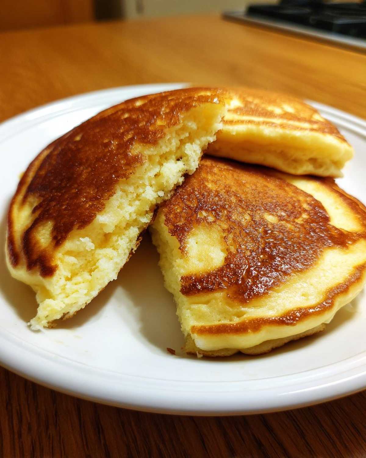 Close-up of fluffy greek yogurt pancakes, one cut open to show the airy interior, served on a white plate.