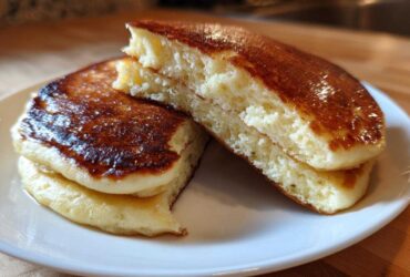 Close-up of fluffy greek yogurt pancakes stacked and cut in half, showing the airy interior and golden-brown tops.