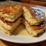 Close-up of a stack of fluffy greek yogurt pancakes cut open, drizzled generously with golden syrup.